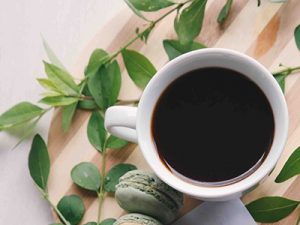 Overview shot of a coffee cup with black coffee surrounded by grean leaves.
