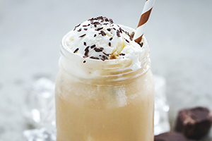 Photo of iced coffee drink with whipped cream and a straw served in a Mason jar.