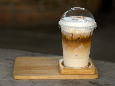 Ice coffee with creamy milk in a plastic glass is on a saucer wood, selective focus, latte art