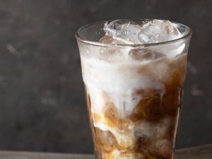 Cold brew coffee with milk on dark background with ice cube and coffee beans.