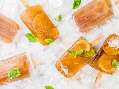 Frozen refreshing drinks, summer cocktail popsicles recipe, cuba libre, cold sweet tea or coffee, with ice, lime and mint leaves on white marble background copy space
