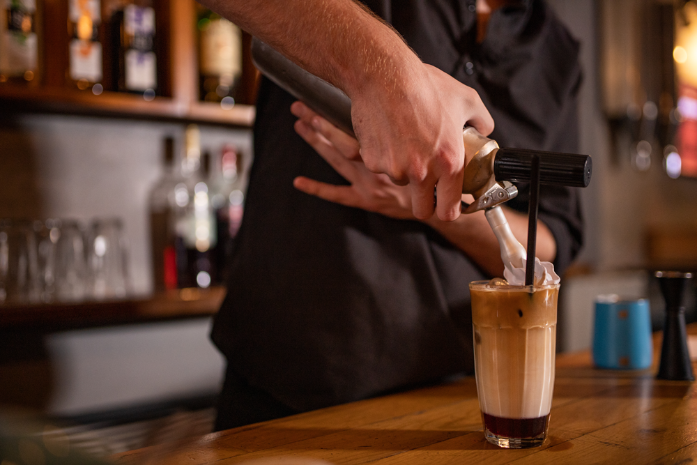 Barista preparing a frappe and adding whipped cream to the top.